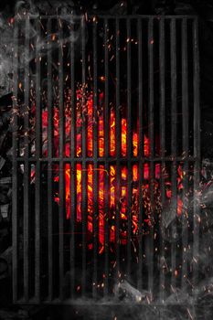 Top view through black barbecue grate of burning coals with sparks and white smoke
