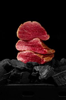 Pieces of lightly seared veal tenderloin on charcoal on black background