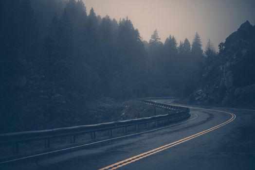 Foggy Curved Mountain Road at Evening. Faded Blue Color Grading.
