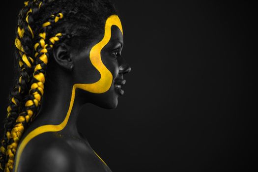Woman on abstract poster with gold face art. Yellow and black body paint. Young girl with bodypaint. An amazing model with makeup.
