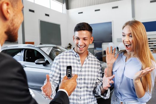 Cherrful young couple at the dealership buying a new car