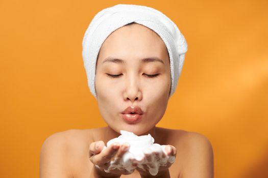 Happy young beautiful Asian blowing foaming cleanser on her hand. Spa concept.