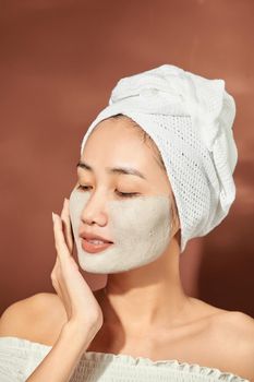 Beautiful woman with clay facial mask over orange background. Beauty treatment and spa concept.