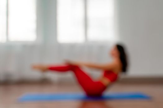In the blur, a young woman in a red tracksuit is doing exercises or yoga in the gym. Serious, calm and focused slender girl. The concept of a healthy lifestyle