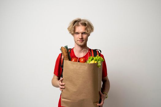 Delivery man employee in red t-shirt uniform hold craft paper packet with food isolated on white background studio.