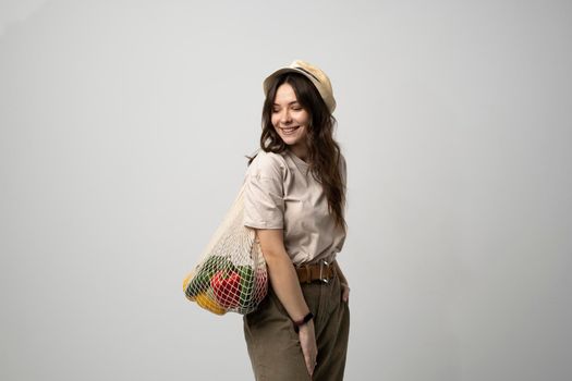 Woman in a beige t-shirt and a hat holding mesh shopping bag with groceries. Conscious consumption. Eco trend. Zero waste concept. Girl carry bag shopper.