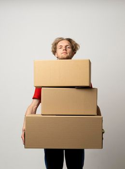 Delivery man in a red uniform holding a stack of cardboard boxes. Courier delivering postal packages over white studio background.