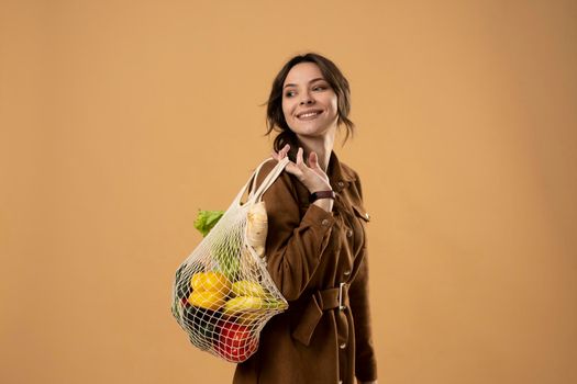 Zero waste concept. Young brunet woman holding reusable cotton shopping mesh bag with groceries from a market. Concept of no plastic. Zero waste, plastic free. Sustainable lifestyle.
