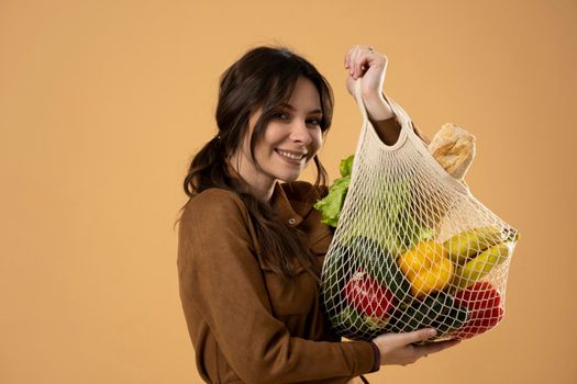 Zero waste concept. Young brunet woman holding reusable cotton shopping mesh bag with groceries from a market. Concept of no plastic. Zero waste, plastic free. Sustainable lifestyle.