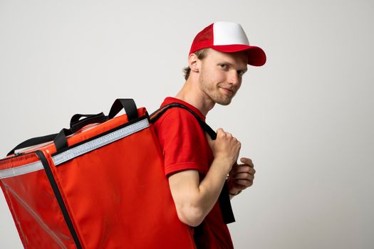 Side view delivery employee man 20s in red cap t-shirt uniform thermal food bag backpack work courier service.
