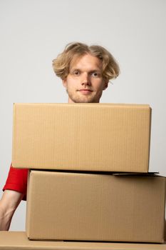 Cheerful delivery man. Happy young courier holding a cardboard boxes and smiling while standing against white background. Delivery man holding pile of cardboard boxes in front of himself.