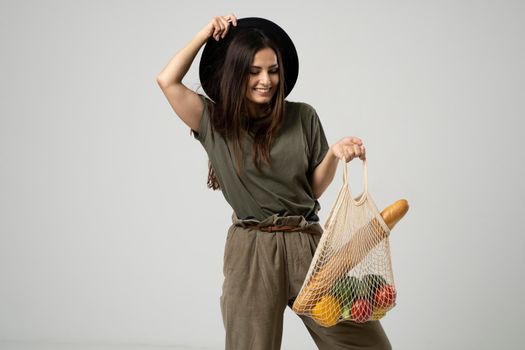 A modern stylish woman with a mesh shopping bag with vegetables against the background of the studio. The concept of healthy nutrition, vegetarianism and ecology. Refusal of plastic bags.