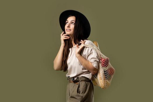 Woman in a beige t-shirt and a hat holding mesh shopping bag with groceries. Conscious consumption. Eco trend. Zero waste concept. Girl carry bag shopper.