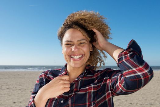happy young woman with hand in curly hair at the beach