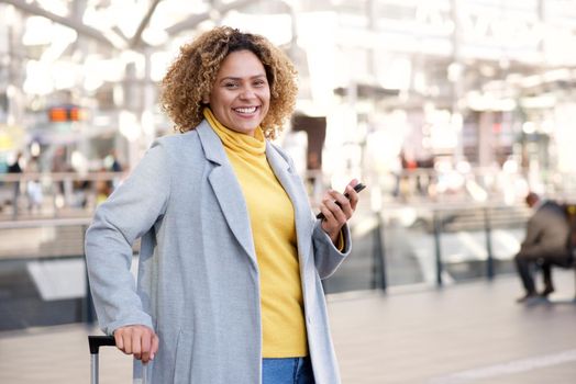 happy african american woman in her 30s smiling with mobile phone at station