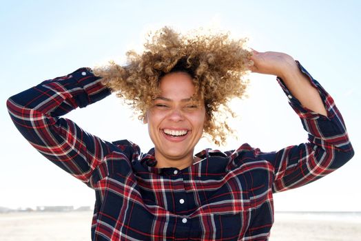 Close up carefree african american woman laughing with hands in hair outdoors