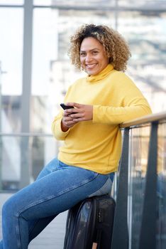 happy travel woman sitting on suitcase at station with mobile phone
