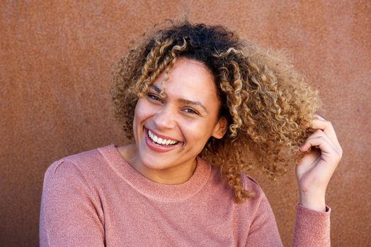 Close up horizontal beautiful african american woman smiling with hand in hair against brown wall