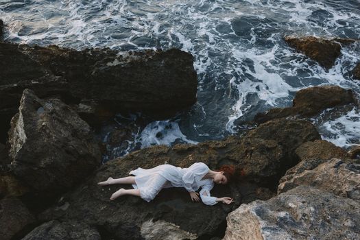 Barefoot woman in a secluded spot on a wild rocky coast in a white dress unaltered