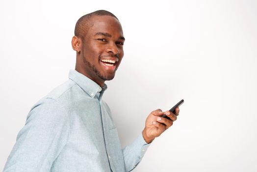 Side of happy young black man holding cellphone by white background