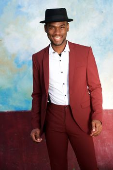 handsome black man in vintage suit and hat smiling by wall