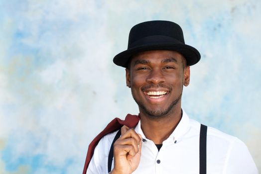 Close up handsome young african american man with suspenders and hat smiling by wall