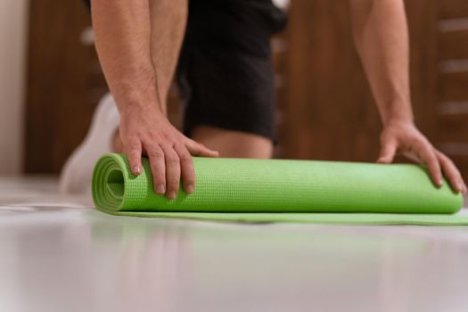 Unwinding roll mat, preparing a place for sports fitness man. Determined guy doing physical training. Strong handsome young man, an a gym
