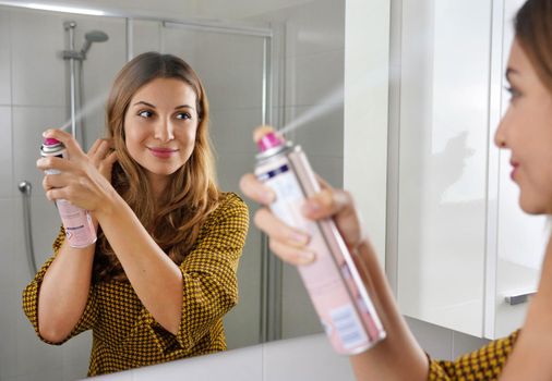 Fast and easy way to covering grey hair with instant spray dye. Young woman applying dry shampoo on her hair before going out.