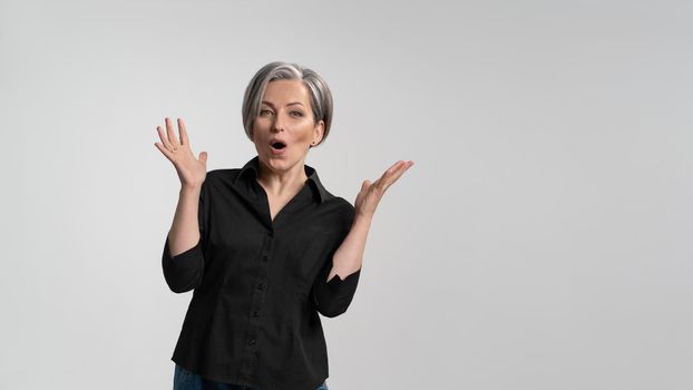 Grey haired mature woman doing a amazement gesture.Pretty mid aged grey haired woman in black shirt isolated on grey background. Human emotions, facial expression concept