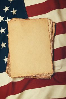 Close up heap of blank vintage yellow paper sheets on old weathered cotton embroidered US national flag, symbol of American history, elevated high angle view, directly above