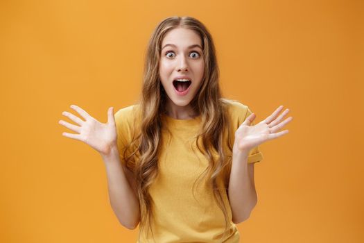 Impressed excited girl describing feelings sharing positive impression gesturing with palms during talk open mouth from amazement and oy communicating lively over orange background