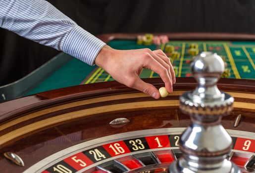 Roulette wheel and croupier hand with white ball in casino