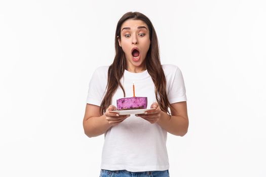 Entertainment, fun and holidays concept. Portrait of funny and cute young caucasian birthday girl making wish, blowing out candle, breathe ait and stare at b-day cake, white background