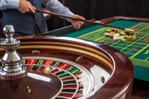 Roulette and piles of gambling chips on a green table.