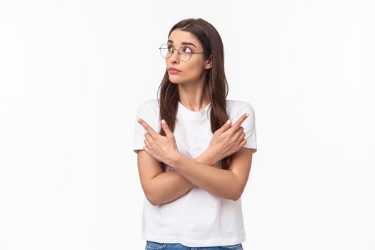 Waist-up portrait of indecisive thoughtful young woman in glasses, 20s female student picking her path, pointing fingers sideways left and right, making decision, thinking over white background