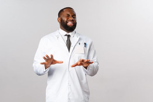 Portrait of disgusted handsome physician or male doctor, african american therapist, grimacing aversion, step back and raise hands in defense from something ugly and disgusting