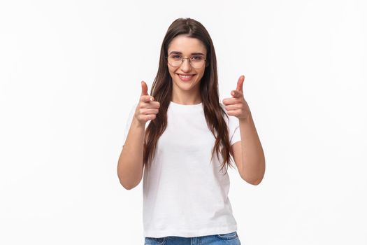 Waist-up of confident, sassy attractive young female coworker in glasses and t-shirt, smiling sly pointing fingers at camera, finger pistols, picking person to join her team or company, recruit