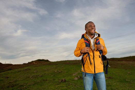 portrait of happy young black man backpacking through fields