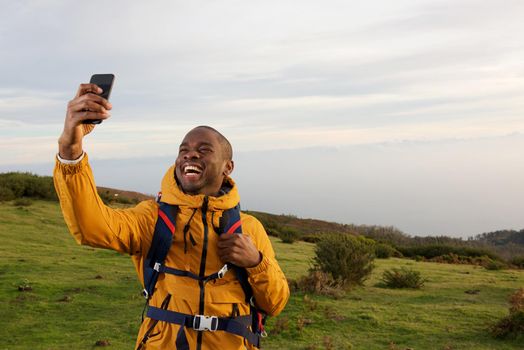 happy african american backpacker taking selfie in nature