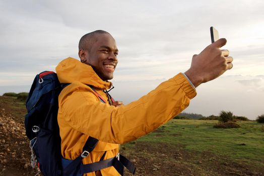 smiling young african american male hiker taking selfie outdoors