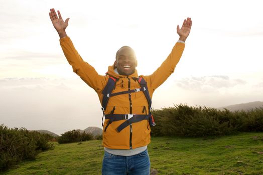 happy african american backpacker standing outdoors with hands raised 