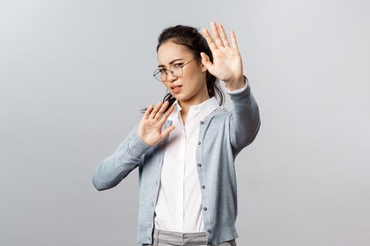 People, emotions and lifestyle concept. Portrait of displeased and disgusted asian woman defending herself from someone coughing close to her, turn away and raise hands from glimmering light