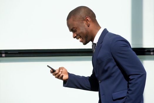 smiling african american corporate businessman walking with cellphone in city
