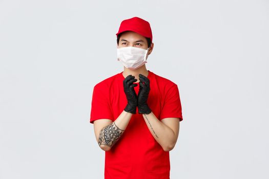 Creative asian delivery guy making plan, sheming something, have interesting thought in mind, steeple fingers in protective gloves, look away pondering idea, protect health with medical mask