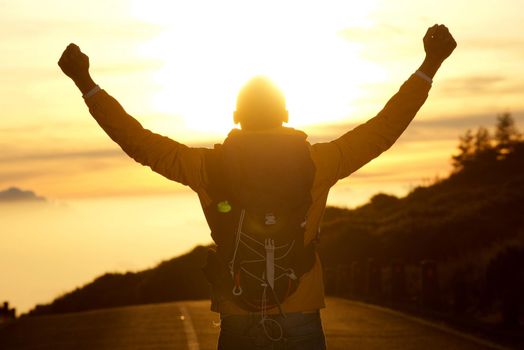  behind of man hiking with arms raised during sunset