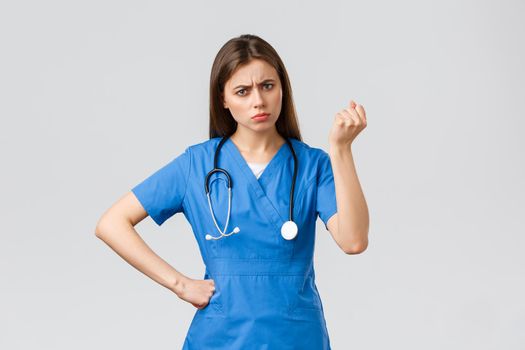 Medical workers, healthcare, covid-19 and vaccination concept. Angry and grumpy young female nurse, doctor scolding young patient breaking quarantine rules, shaking fist in threat