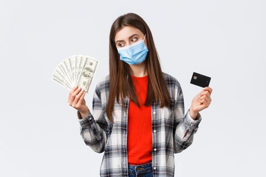 Money transfer, investment, covid-19 pandemic and working from home concept. Pleased young woman in medical mask earn cash, smiling as look at dollars and show credit card