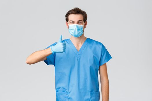 Coronavirus outbreak, healthcare workers fighting disease, hospitals concept. Friendly doctor in blue scrubs asking to support nurses and medical workers during covid-19, show thumb-up