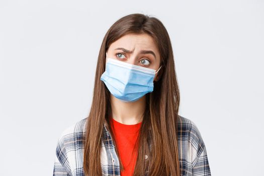 Coronavirus outbreak, leisure on quarantine, social distancing and emotions concept. Thoughtful and intrigued woman in medical mask, looking left with interest, thinking, white background.