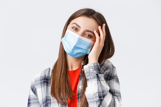Coronavirus outbreak, leisure on quarantine, social distancing and emotions concept. Close-up of tender happy young woman in medical mask, tilt head, flirting and playing with hair